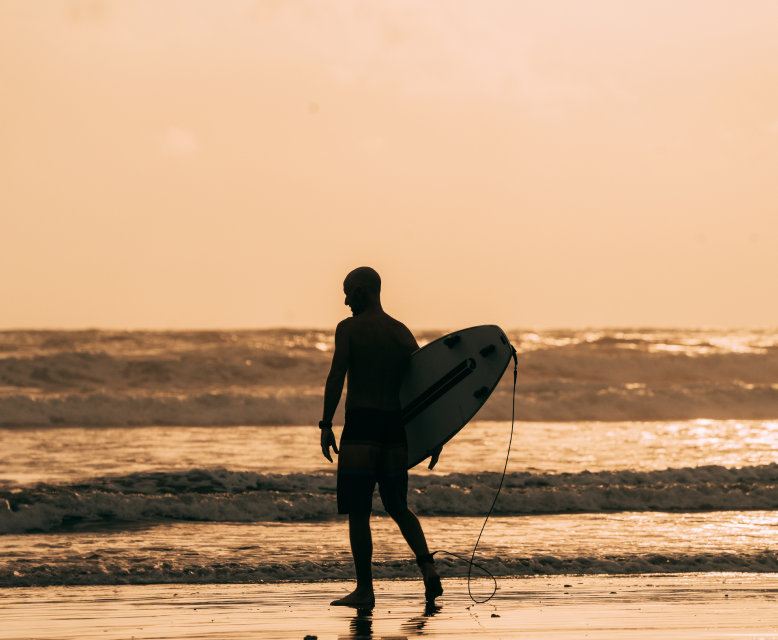 Person with a surfboard watching the waves at sunset, capturing the thrill and connection with the ocean.
